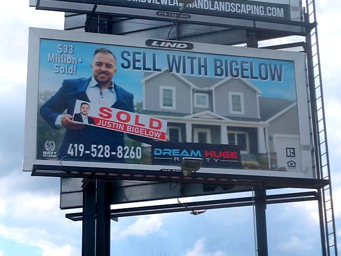 Photo of a Lind Billboard with an image of a reltor and the text "Sell with Justin Bigelow-Dream Huge Realty"